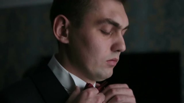 Handsome stylish groom adjusts his blak suit close up