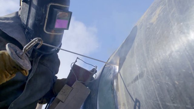 Industrial worker welding steel duct pipe by using metal torch in sunny winter day