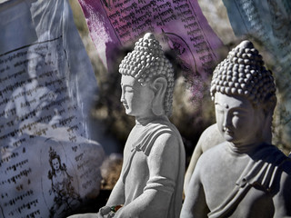 Buddhist figures made of cement sitting in meditation with prayer offerings and prayer flags
