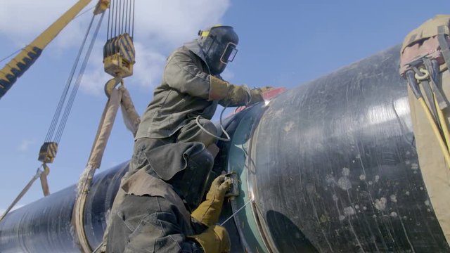Industrial workers welding steel duct pipe by using metal torch in sunny winter day