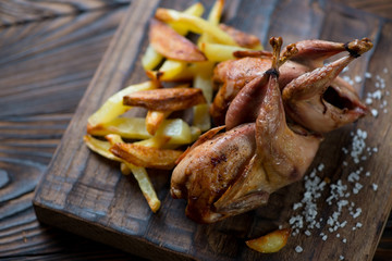 Close-up of two whole baked quails and potato, selective focus