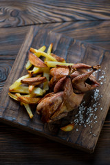 Baked quails and potato on a rustic wooden serving board