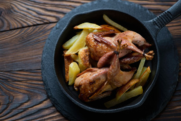 Whole baked quails and potato in a frying pan, closeup, top view