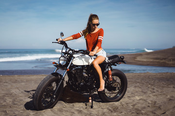 Naklejka na ściany i meble young pretty hipster girl Biker girl sitting on vintage custom motorcycle Biker girl sitting Outdoor lifestyle portrait. jeans short denim, fashion style