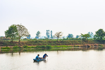 The fisherman in the boat use net to catch fish in the river.