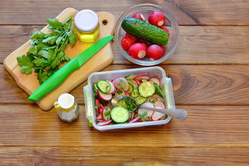 Vegetables in a glass dish, a plastic container with sliced vegetables, a cutting Board, a kitchen knife, olive oil, salt, parsley on a wooden table
