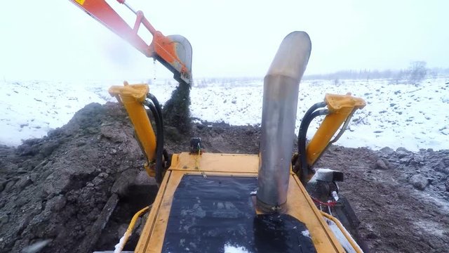 Bulldozer and Excavator machine working with ground on snow winter day. View from cabin
