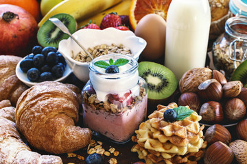 Health breakfast - with homemade granola, waffles, muffins,almond,hazelnuts,various fresh fruits, berries and milk on old wooden table. Health food concept .Top view.