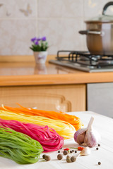 Multicolored pasta on a wooden table in the kitchen background