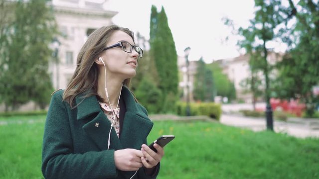 Girl in coat listening to music from phome on the outdoor background 4k