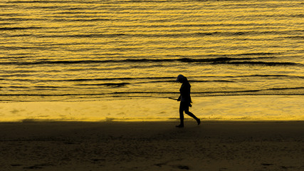 Fototapeta na wymiar Silhouette woman walking along the Hua Hin beach with golden sea background, Thailand