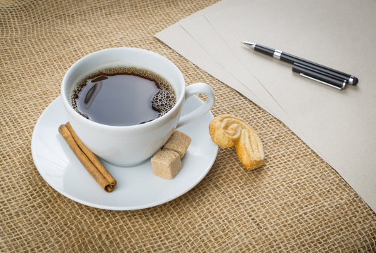 Cup of coffee, cookie, pen and paper on sackcloth background