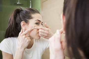 Obraz na płótnie Canvas Young woman squeeze her acne in front of the mirror. Skin problems,woman hiving pimple