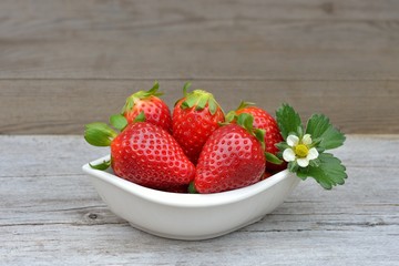 Red strawberry in a bowl, on old wood.