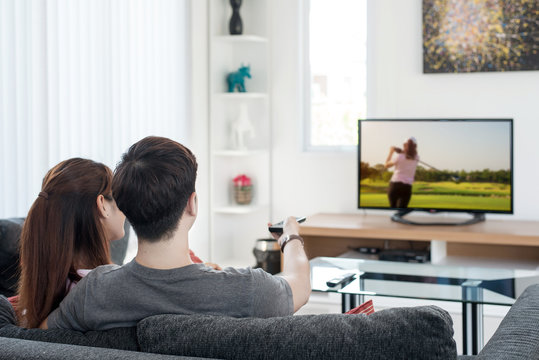 Young Asian Couple Waching Golf Sport On Tv At Home