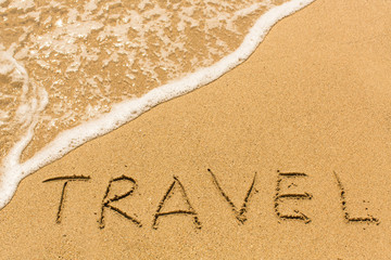 Travel - inscription by hand on yellow beach sand.