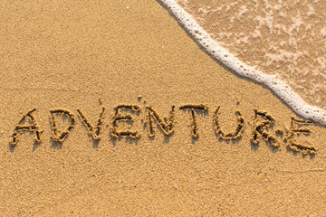 Adventure - inscription by hand on yellow beach sand.