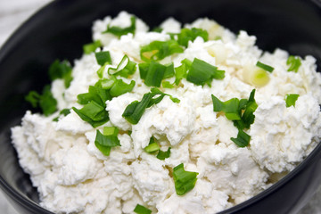 Cottage cheese with chives in black ceramic bowl 