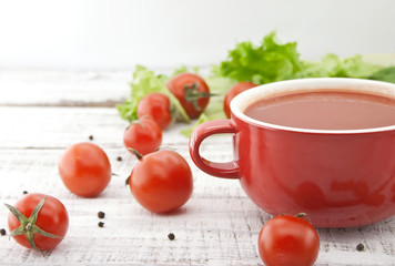Tomato soup in red ceramic bowl on rustic wooden background. 