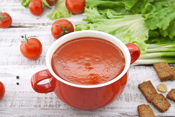 Tomato soup in red ceramic bowl on rustic wooden background. 
