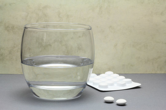 Two painkiller tablets from a blister pack with a glass of water