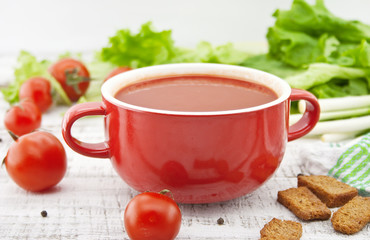 Tomato soup in red ceramic bowl on rustic wooden background. 