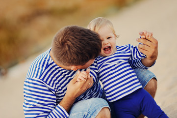 Папа и маленькая дочь в полосатых майках играют на пляже