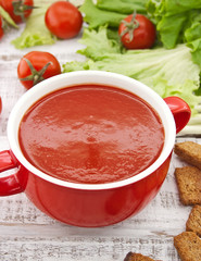 Tomato soup in red ceramic bowl on rustic wooden background. 