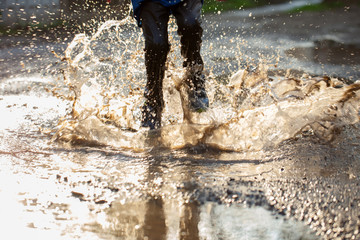 Little boy splashing in a mud puddle, jumping into a puddle
