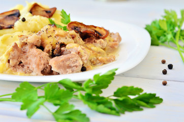 Mashed potatoes with meat and mushrooms on a wooden table. Sprigs of parsley and pepper grains close to the plate