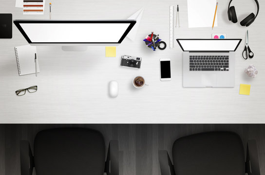 Work desk with computer and laptop with white isolated screens. Paper, camera, coffee, smart phone, notepad, pens, glasses, calculator, scissors on table. Top view.