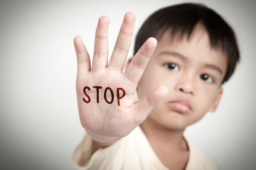 sad face of asian kid and hand raise stop written on his hand.