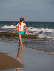 Fototapeta na wymiar Blonde little girl in colorful swimsuite running along seashore