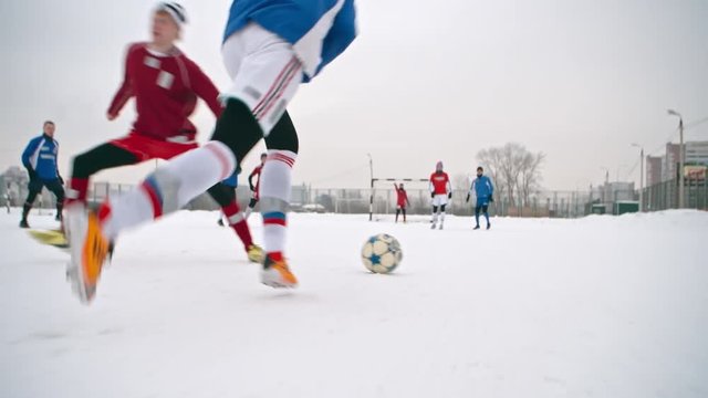 Soccer player handling a ball, getting around opposing players and unsuccessfully attempting taking a shot on goal during  a play on snow-covered winter field 