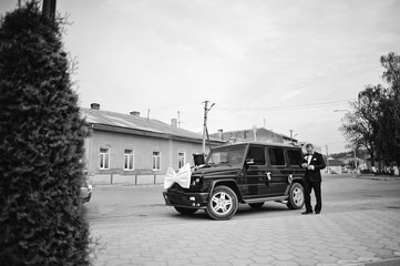 Stylish groom near maffia car at wedding cortege