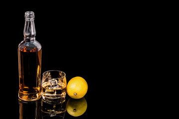 Bottle and glass whiskey with lemon on black background