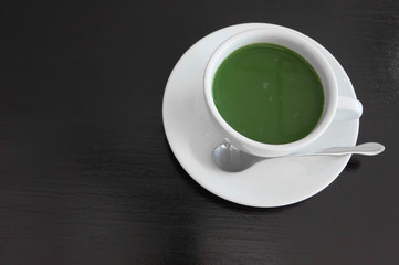 hot milk green tea in white teacup , black wooden background