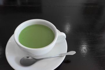 hot milk green tea in white teacup , black wooden background