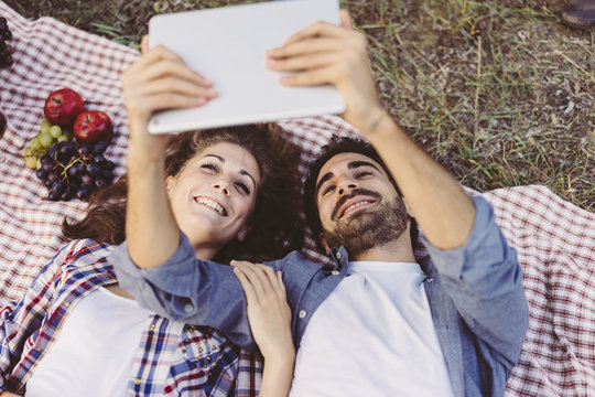Young couple in love doing a picnic outdoors and using a tablet