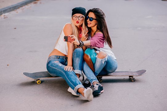 two young friends holding a skateboard and sending a kisses . Su