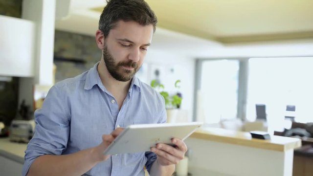 Man at kitchen countertop working on tablet from home