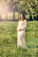 Expecting mom touching her abdomen while outdoors on sunny day