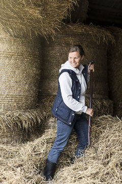 Smiling woman moving hay with pitchfork