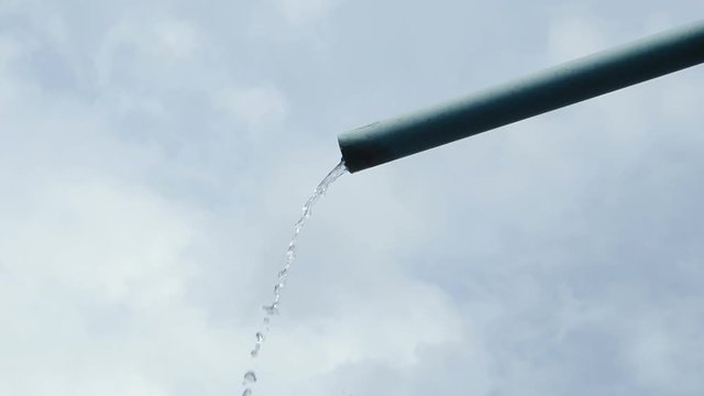 Water flowing from pipe against cloud sky background.
