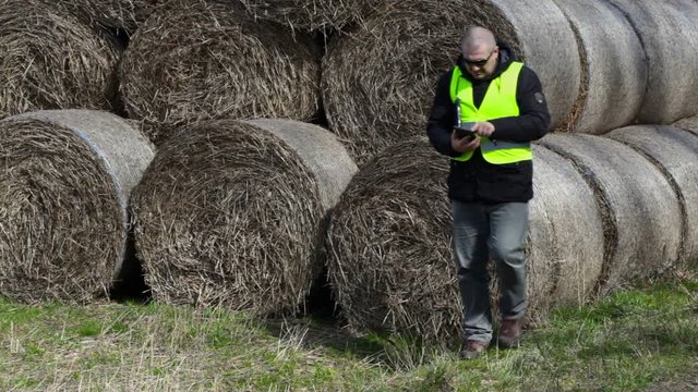 Farmer with tablet PC numbering the hay bales