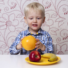 Fototapeta premium The three-year boy eats a yellow grapefruit