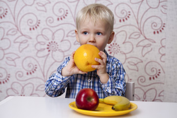 Fototapeta na wymiar The three-year boy eats a yellow grapefruit