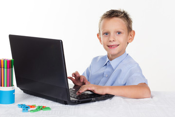 Happy schoolboy is doing homework on laptop