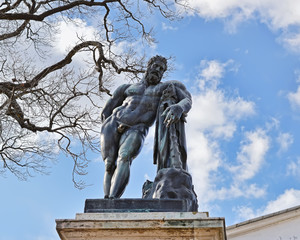 Бронзовая скульптура Геракла на пьедестале на фоне неба.