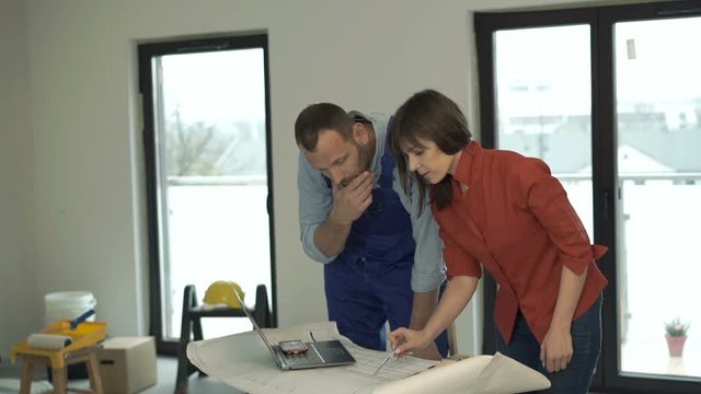 Woman and male worker talking and working with blueprints at her new home
